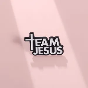 Macro shot of Team Jesus enamel pin with black and white cross on a pink background