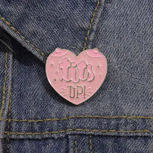 Close-up of heart enamel pin with tits UP text on dark blue denim jacket collar