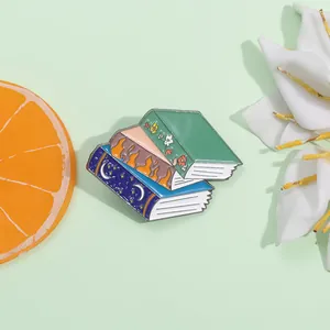 Detailed view of stacked book enamel pin featuring moon and flower designs on light green backdrop
