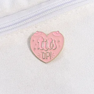 Detail of pink heart-shaped enamel pin with Tits UP! text on white canvas material
