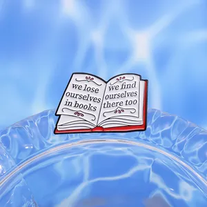 Detail of an open book enamel pin with engraved quote on light blue background