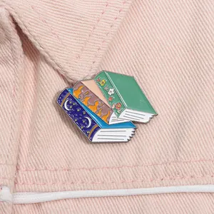 Detail of stacked fantasy book enamel pins on pink denim fabric for book lovers