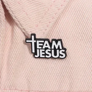 Religious Jesus enamel pin with black and white cross design on pink denim background