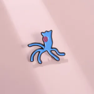 Detailed close-up of a blue cartoon enamel pin with pink button eyes on a soft pink surface