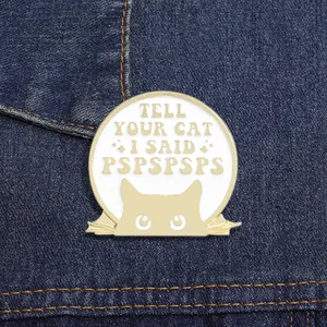 Close-up of Tell Your Cat I Said Pspspsps enamel cat pin on blue denim fabric