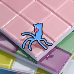 Close-up of a blue cartoon rag doll enamel pin with a pink button eye on mosaic tiles
