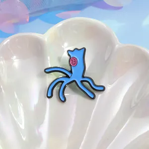 Detail of blue cartoon enamel pin with pink button eyes resting on a pearl shell tray
