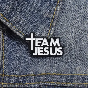Detail showing Team Jesus enamel pin with a white cross on a denim jacket collar