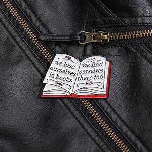 Detailed close-up of an open book enamel pin with red accents on a black leather jacket