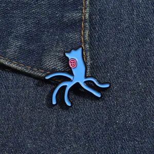 Cartoon blue alien enamel pin with pink button eyes pinned on a denim jacket background