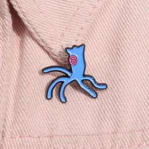 Detailed view of a blue enamel pin with a pink button eye on pink denim fabric