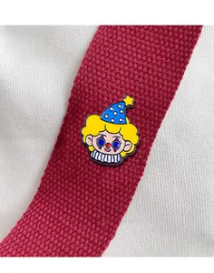 Macro shot of cute cartoon clown enamel pin on red strap with bright colorful details