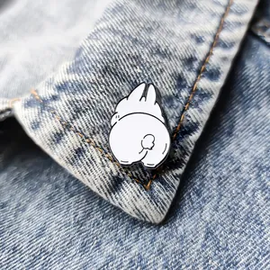 Close-up of cute cartoon white bunny enamel pin with round tail on blue denim jacket