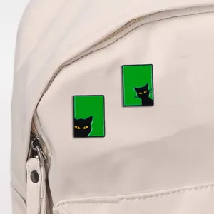 Lot de deux pins chat noir émaillés avec fond vert sur un sac à dos en toile blanc