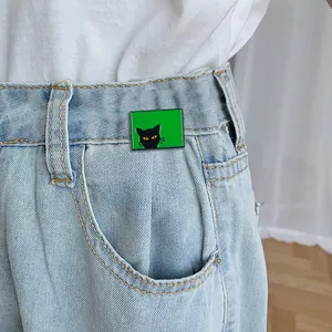 Détail d'un pin's chat noir créatif sur fond vert porté sur un vêtement en jean