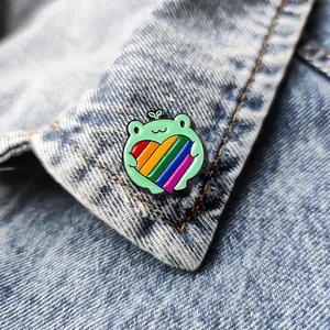Detailed close-up of a cartoon frog enamel pin with a rainbow heart on denim fabric