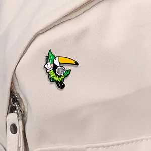 Vue détaillée du pin's toucan en émail avec fleur rose sur une lanière de sac en toile