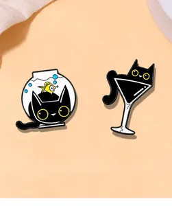 Detail shot of cute black cat enamel pins featuring designs in fishbowl and martini glass