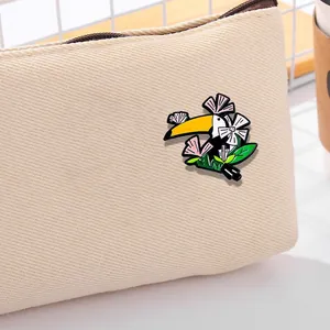 Broche en émail toucan mignon avec fleurs et feuilles fixée sur un sac en toile beige