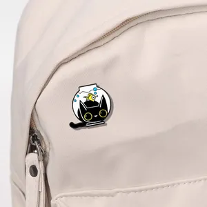Close-up of a cartoon black cat enamel pin attached to a beige canvas backpack strap