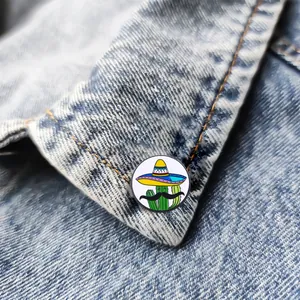 Enamel cactus pin with sombrero and mustache on blue denim fabric background