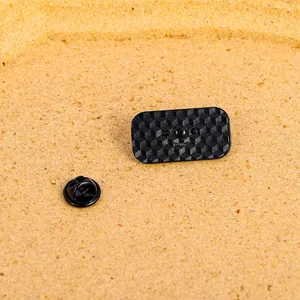 Dettaglio del retro della spilla in metallo nero con texture geometrica e chiusura a farfalla