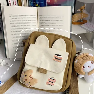 Canvas crossbody bag with rabbit ears, book-themed badges, and a cartoon cat pendant