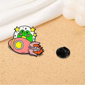 Cute enamel pin featuring a cartoon frog riding a pink rocket with yellow stars