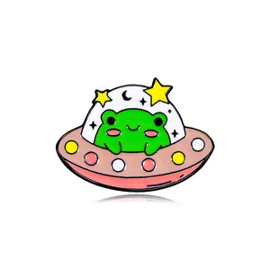 Cute green frog in a pink UFO enamel pin with stars and crescent moon on white background