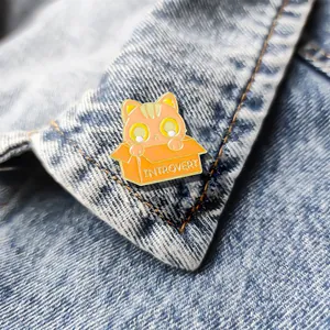 Pin's en émail chat orange dans un carton avec texte Introvert sur veste en jean