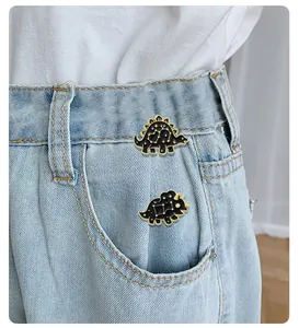 Detailed view of black enamel dinosaur pins with gold constellations on blue denim fabric