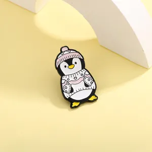 Dettaglio di una spilla smaltata con pinguino che indossa cappello e maglione rosa