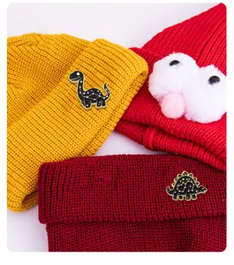 Detail of enamel black dinosaur pins with gold constellations on knitted beanies
