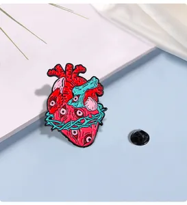 Macro view of anatomical heart enamel pin with eyes and mint green thorns on silk