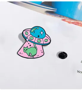 Detail view of a cartoon UFO cat enamel pin with a pink beam on a white background