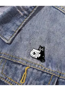 Détail d'un pin's en émail chat noir buvant dans un bocal, porté sur une veste en jean