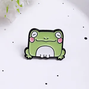 Detailed close-up of a cute green cartoon frog enamel pin on a clean white background