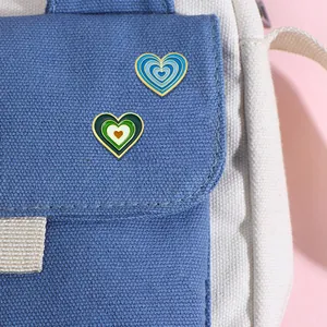 Deux pin's en émail en forme de cœur bleu et vert fixés sur un sac à dos en toile