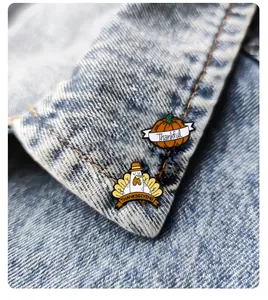 Close-up of Thanksgiving enamel pins featuring a pumpkin and turkey on a denim jacket