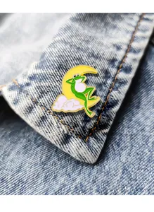 Detail of funny green frog reclining on a yellow moon enamel pin on denim jacket