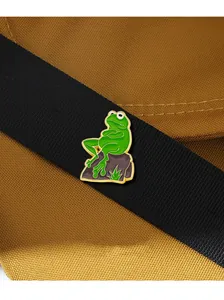 Detail of Sad Frog enamel pin on a black canvas strap with golden metal outlines