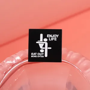 Macro detail of square black enamel pin featuring Enjoy Life and Eat Out More Often text