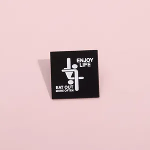 Close-up of square black enamel pin featuring Enjoy Life Eat Out More Often text