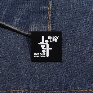 Close-up of black enamel square pin with 'ENJOY LIFE' text on denim jacket
