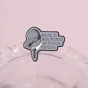 Detailed view of enamel dolphin brooch wearing headset with funny quote on pink background