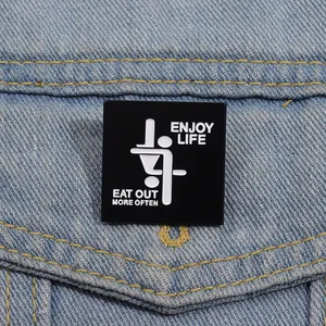 Close-up of square black enamel pin with Enjoy Life text on a denim jacket pocket