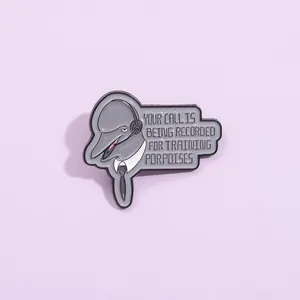 Macro detail of humorous dolphin enamel pin with training porpoises text on purple background