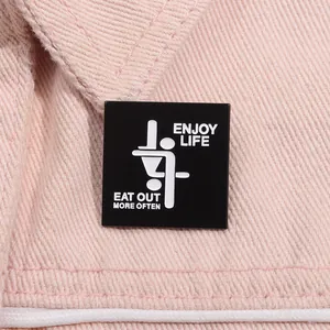 Macro detail of a square black enamel pin with white text on pink denim fabric