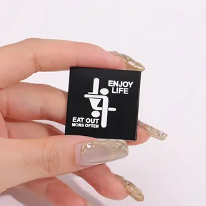 Detail of square black enamel pin featuring creative white lettering and graphic motif