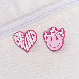 Detail of pink Be Kind heart and cowboy hat smiley face enamel pins on white canvas